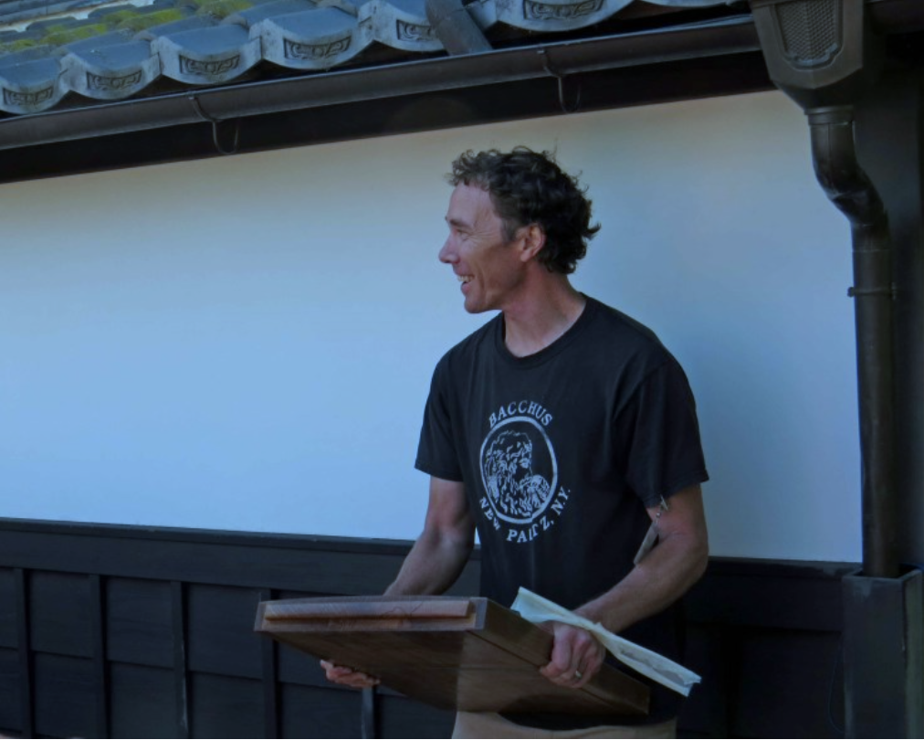 Andrew Hunter holding a rather large Japanese hand plane (ooganna) while standing outside next to a building.